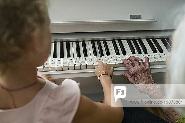 Grandmother and granddaughter playing piano at home