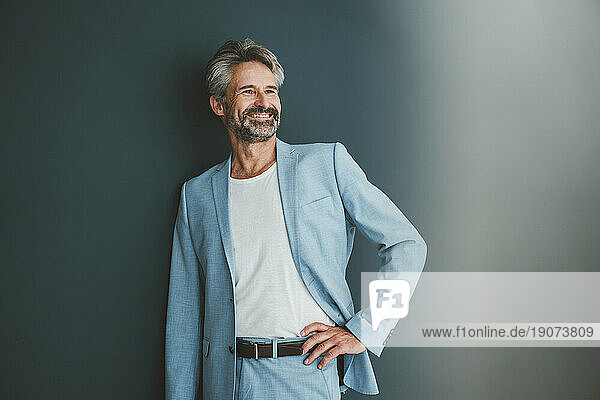 Happy businessman standing with hand on hip against teal background