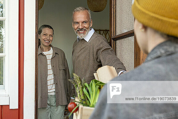 Happy couple receiving groceries from delivery person at door