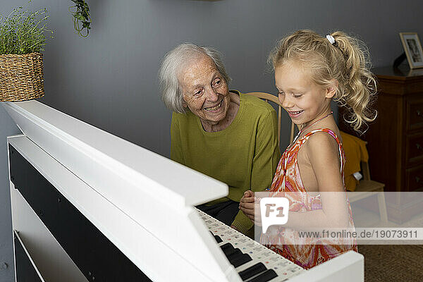 Smiling grandmother playing piano with granddaughter at home