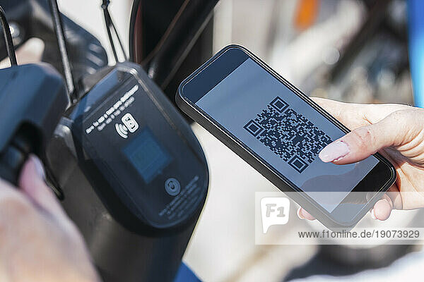 Hands of woman renting electric bicycle through mobile phone app