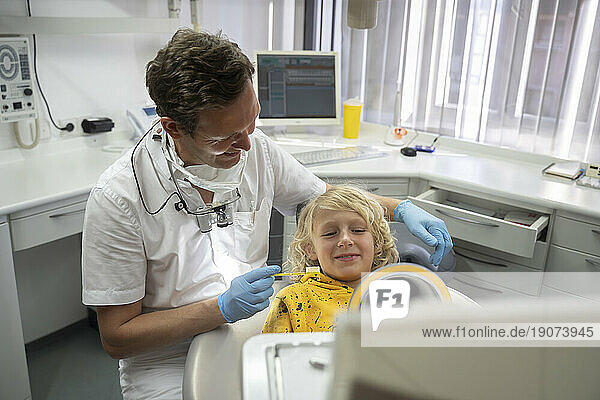 Smiling boy looking in hand mirror at dental clinic