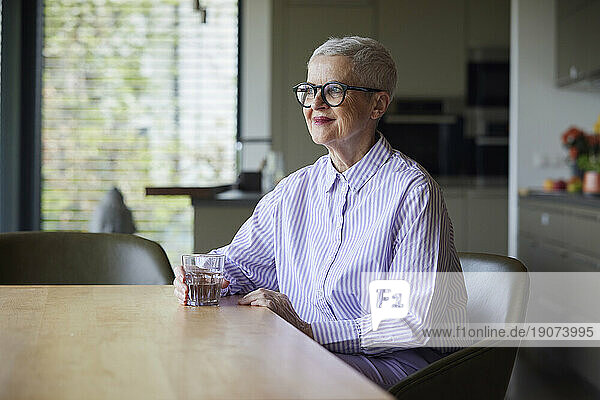 Confident senior woman sitting at table at home