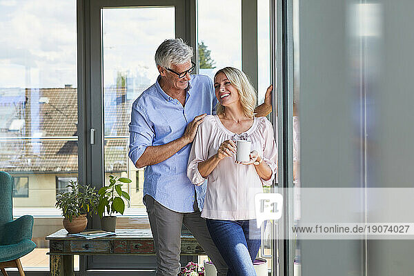 Smiling mature couple relaxing at home at the window