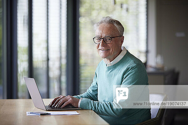 Portrait of smiling senior man using laptop at table at home