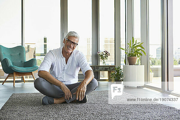 Portrait of smiling mature man relaxing sitting on carpet at home