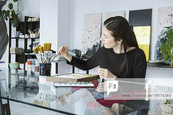 Artist selecting paintbrush working in workshop