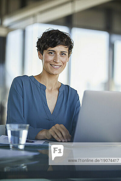 Portrait of confident businesswoman sitting at desk in office with laptop