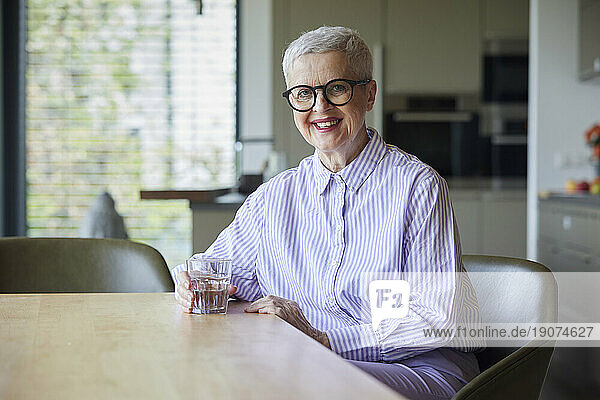 Portrait of smiling senior woman sitting at table at home