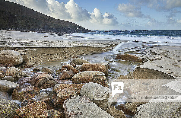 A stream cuts through sand and rocks as it makes its final dash to the sea  Portheras Cove  a remote cove on the Atlantic Coast  near Pendeen  in the far west of Cornwall  England  United Kingdom  Europe