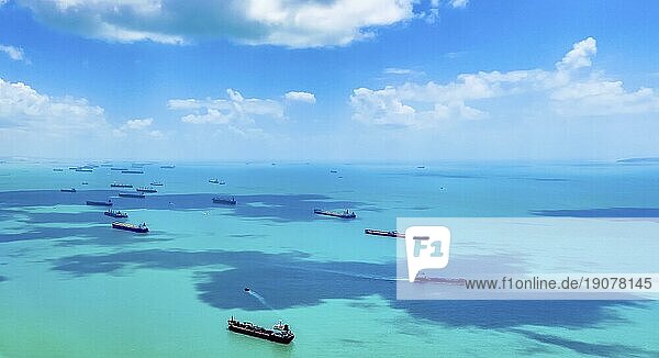 Luftaufnahme von Fracht Fracht oder Containerschiffen auf der Straße in der Singapore Strait. Blauer Himmel  schöne Wolken  azurblaues klares Meerwasser. Frachtschiffe vor Anker und warten auf die Einfahrt in den geschäftigsten Hafen in Südostasien. Kopierraum. Internationaler Handel