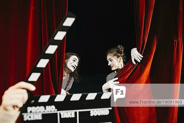 Person s Hand hält Klappe vor zwei Pantomime Künstler Durchführung roten Vorhang