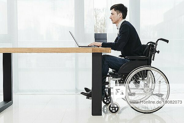Seitenansicht junger Geschäftsmann im Rollstuhl sitzend mit Laptop neues Büro