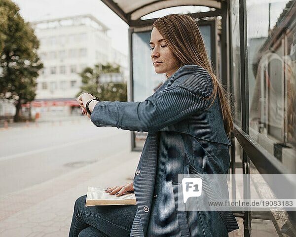 Frau wartet auf Bus mit Buch auf dem Schoß