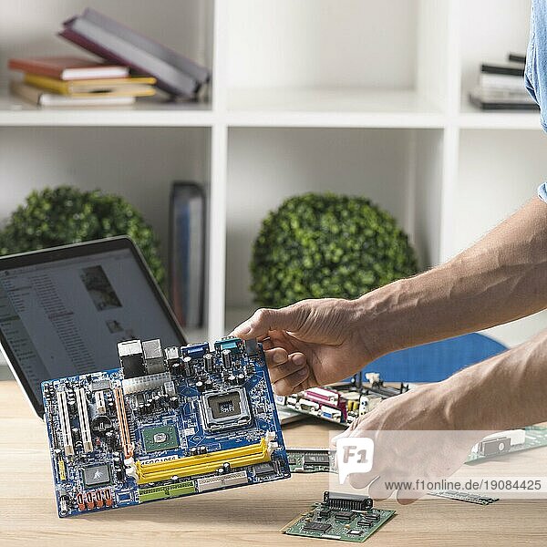 Nahaufnahme eines männlichen Technikers  der ein modernes Computermotherboard vom Tisch hält