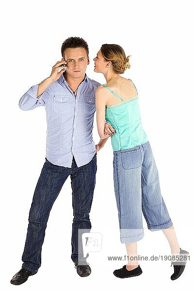Junges  attraktives  lässiges Paar  Mann telefoniert  Frau flüstert ihm etwas ins Ohr  vor weißem Hintergrund