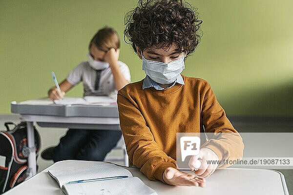 Vorderansicht Kind mit medizinischer Maske beim Desinfizieren der Hände Klasse
