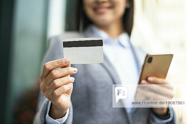 Lächelnde Geschäftsfrau mit Smartphonekreditkarte im Freien