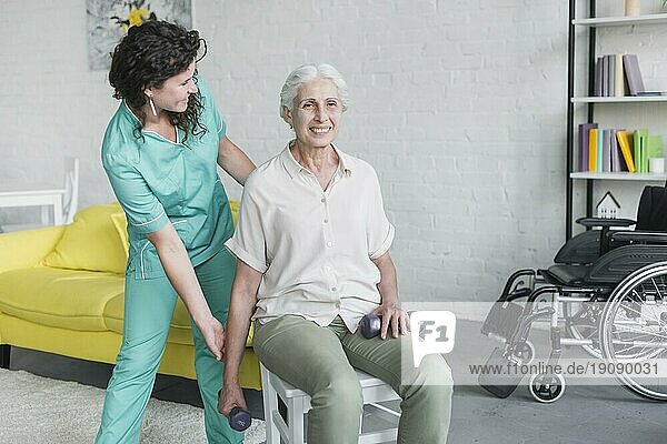 Junge hübsche Krankenschwester  die einer alten Frau bei ihrer Therapie hilft