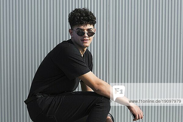 Junge ethnische lockige Mann Sonnenbrille schwarze Kleidung gegen graue Wand