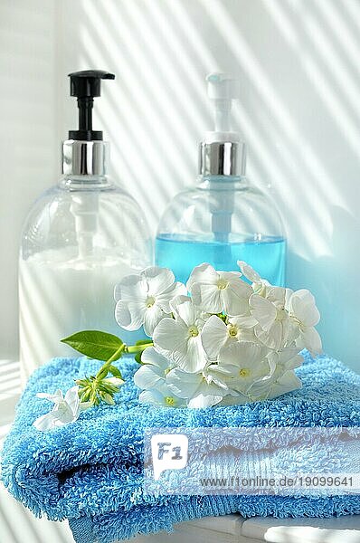 Symbolisch Wellness. Blaues Handtuch mit weißer Blüte und Seifen- und Cremspender im Hintergrund