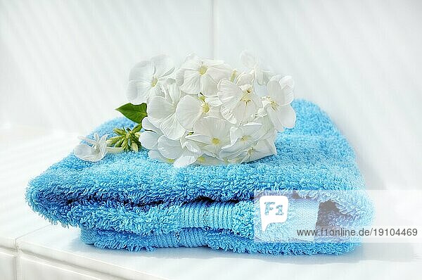 Blaues Handtuch mit weißer Blüte liegende auf einem Kachelabsatz