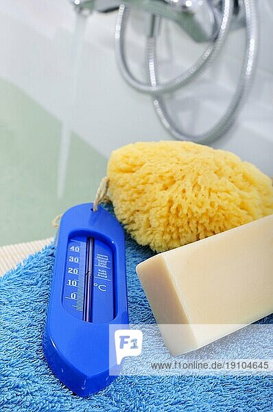 Handtuch  Seife  Schwamm und Thermometer vor gefüllter Badewanne