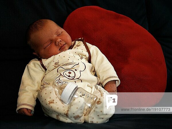 Schlafendes Baby mit Fläschchen auf Sofa mit Kissen