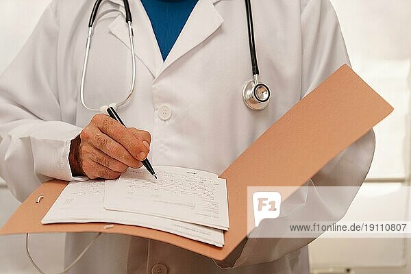Unbekannter Arzt in weißem Kittel und mit Stethoskop schreibt ein Rezept für einen Patienten in seinen Ordner