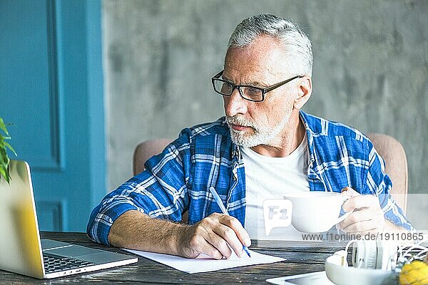 Älterer Mann mit Laptop und Stift  der Notizen macht