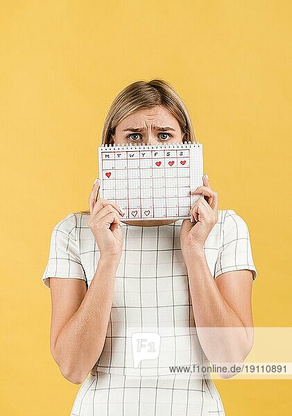 Schockierte Frau bedeckt ihr Gesicht mit Periodenkalender