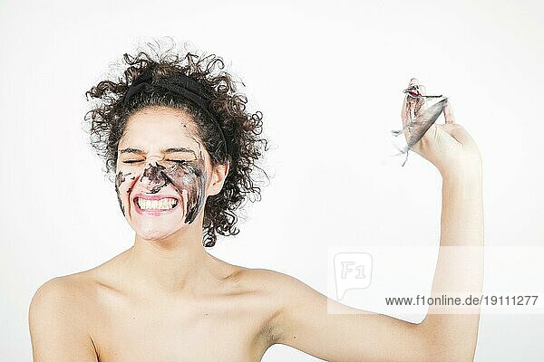 Lächelnde glückliche junge Frau beim Entfernen der Gesichtsmaske vor weißem Hintergrund