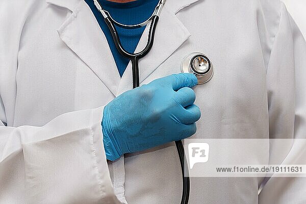 Nahaufnahme eines Arztes mit blauen Latexhandschuhen und einem Stethoskop in der Hand  der sich selbst auskultiert