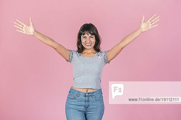 Fröhliche Frau mit offenen Armen  die eine rosa Brustkrebsschleife auf rosa Hintergrund trägt. Sieg über Brustkrebs Konzept