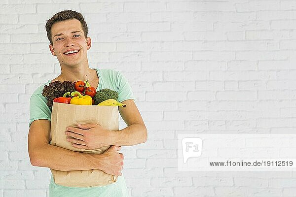 Lächelnder junger Mann hält frisches Gemüse Früchte Lebensmittelgeschäft Papiertüte