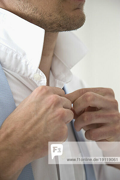 Close up of a young man buttoning white shirt