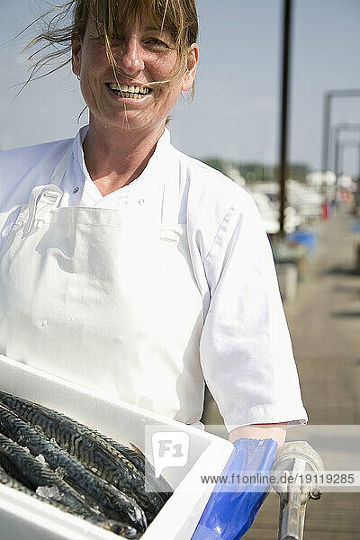 Portrait of smiling fishmonger holding a white container full of fish