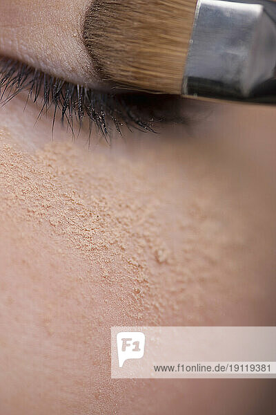 Woman applying eye make-up with eyeshadow brush and makeup powder under eye