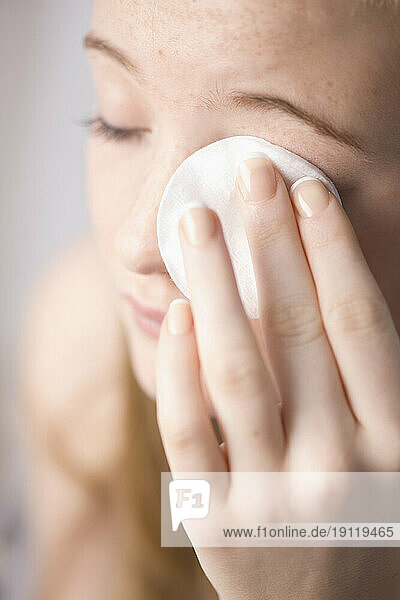 Close up of young woman removing make up with white cotton pad