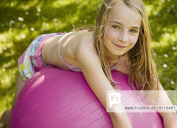 Portrait of young blonde girl lying on pink ball smiling