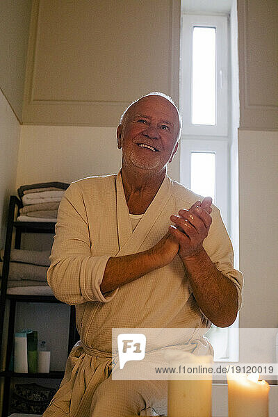 Lächelnder älterer Mann sitzt bei angezündeter Kerze im Badezimmer zu Hause