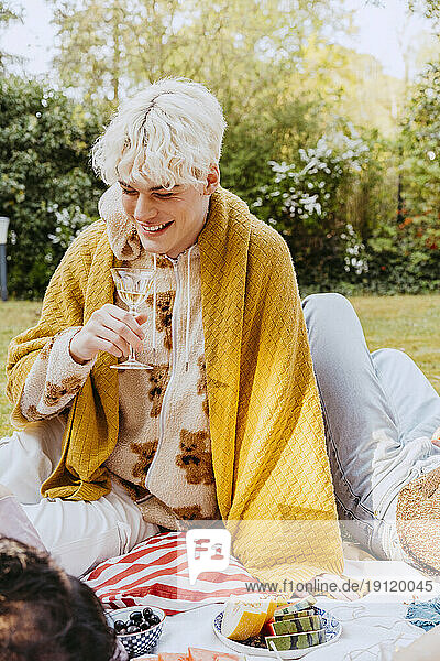 Smiling gay man with blanket sitting in back yard during dinner party