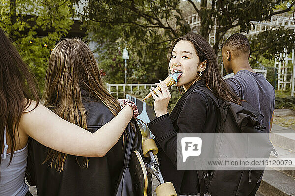 Junge Frau schaut zurück  während sie ein Eis isst und mit Freunden in der Stadt spazieren geht