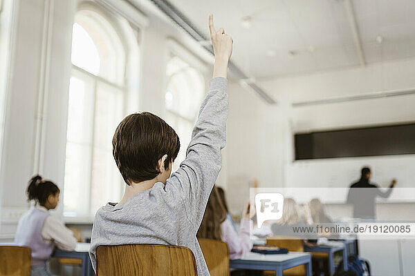 Junge hebt die Hand  während er eine Vorlesung im Klassenzimmer besucht