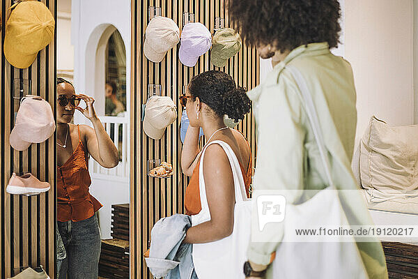 Frau probiert Sonnenbrille  während sie neben einem Mann in einer Modeboutique steht
