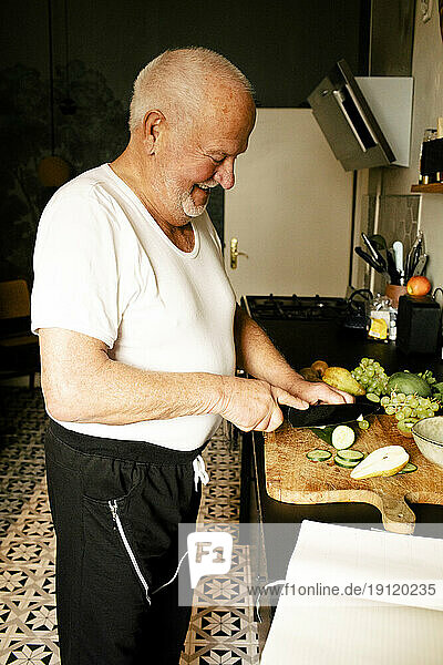 Glücklicher älterer Mann hackt Gemüse in der Küche zu Hause