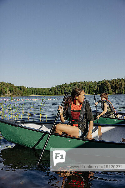 Girl looking away while sitting in kayak on lake at summer camp