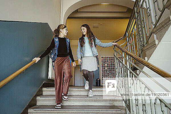 Lächelnde Freundinnen  die von einer Treppe im Schulgebäude heruntergehen