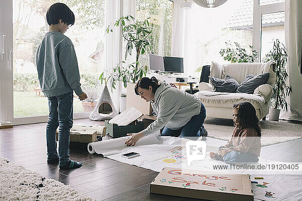 Mutter mit Sohn und Tochter  die im Wohnzimmer zu Hause auf einem Stoff zeichnen