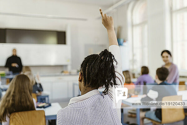 Rückansicht einer Studentin  die während einer Vorlesung im Klassenzimmer die Hand hebt